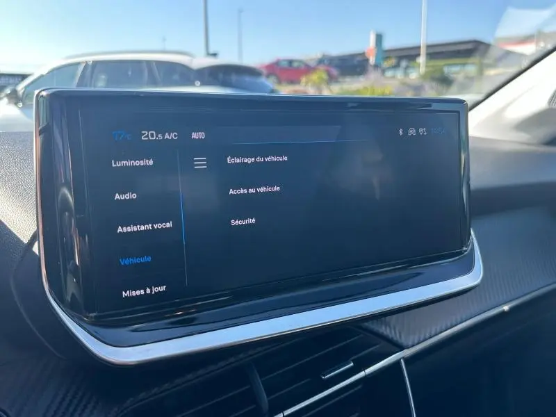 Écran tactile central du tableau de bord du Peugeot 208 gris 2024 affichant les réglages du véhicule en plein jour