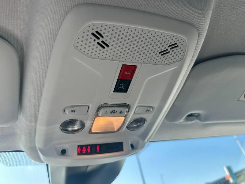 Plafonnier intérieur du Peugeot 208 gris 2024, avec boutons d’éclairage et alerte SOS visibles sous ciel bleu.