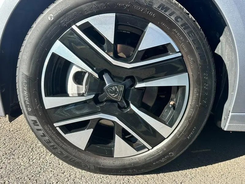 Gros plan sur la jante noire et argentée d'une Peugeot 208 gris 2024, mettant en valeur le logo lion central.