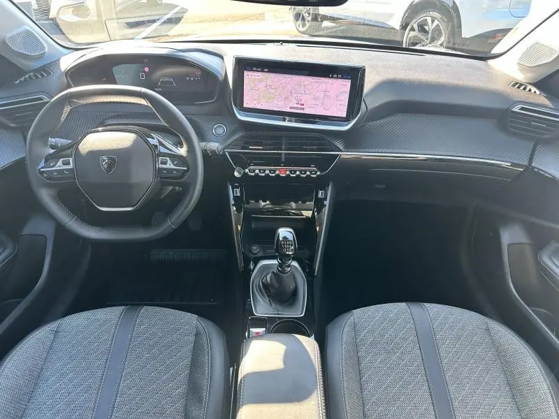 Vue intérieure avant du Peugeot 208 gris 2024, avec tableau de bord numérique, écran tactile et levier de vitesse manuel.