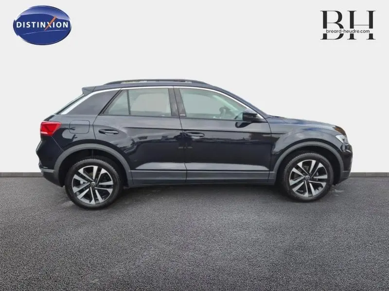 Profil côté gauche d'un Volkswagen T-Roc gris Urano 2021 avec jantes alliage et barres de toit visibles.