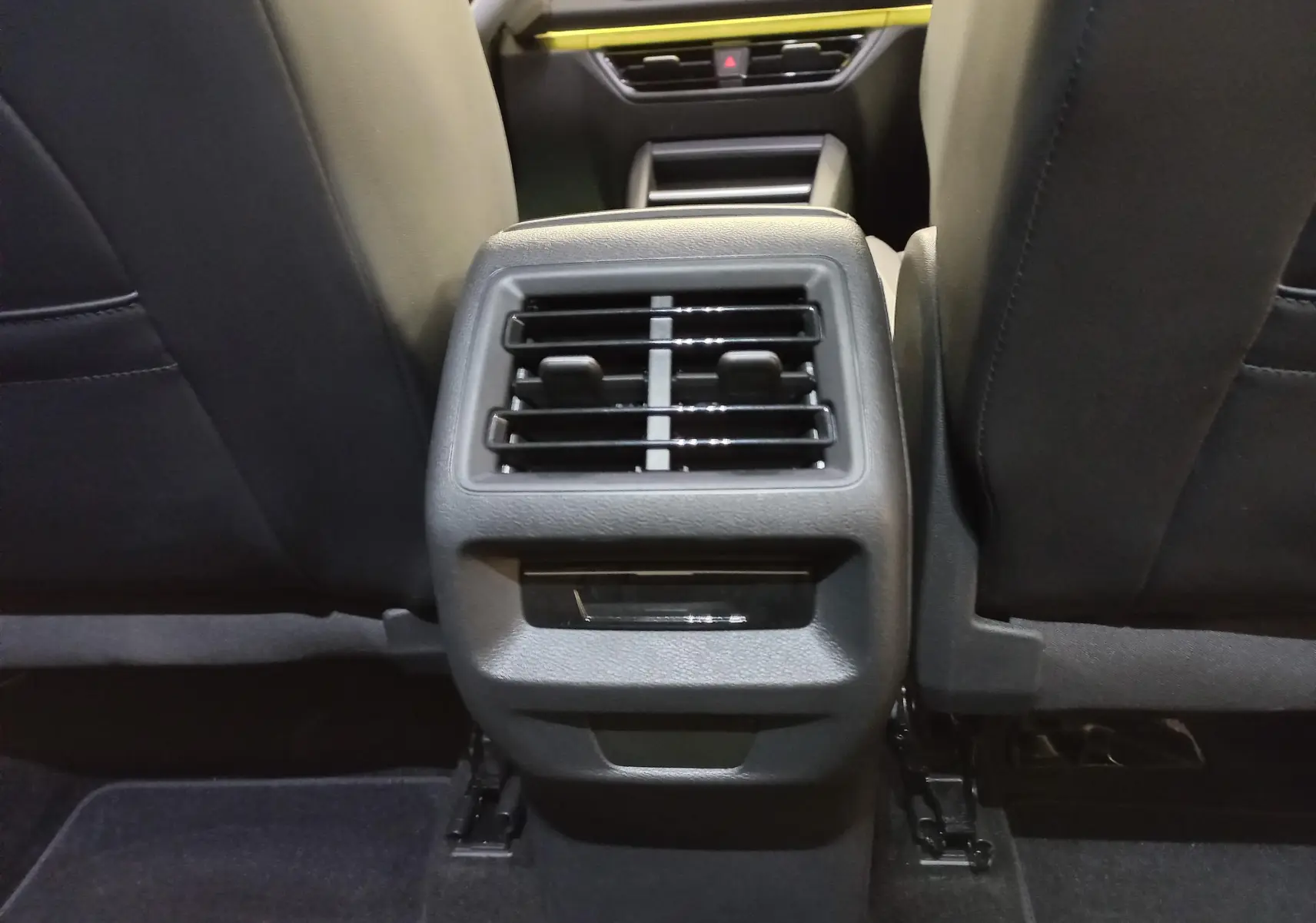 Buses d'aération arrière entre les sièges avant noirs du Volkswagen Tiguan 2025, intérieur sobre et fonctionnel.