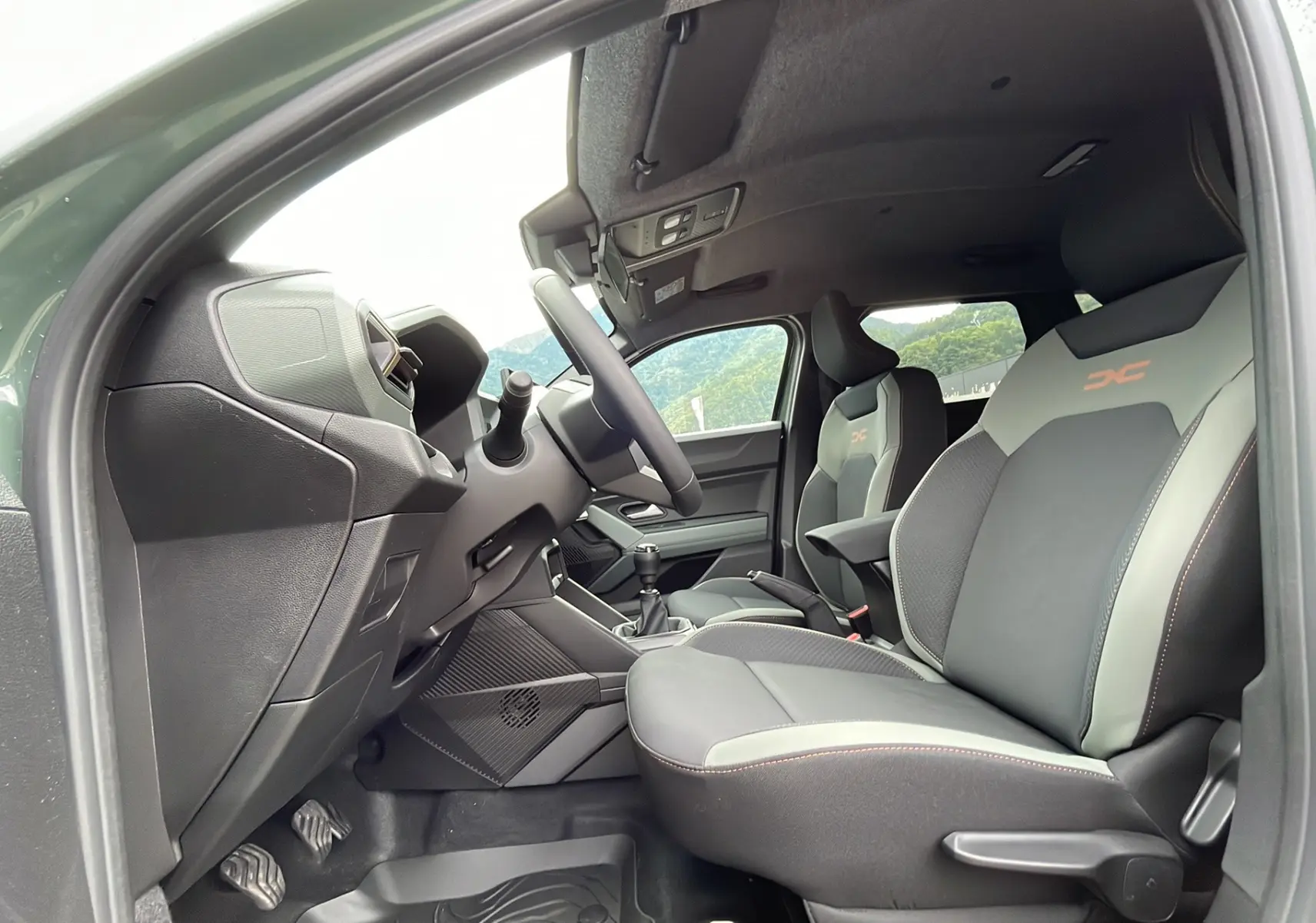 Vue intérieure côté conducteur du Dacia Duster 2025 kaki lichen, sièges avant bi-ton avec logo orange et volant cuir.