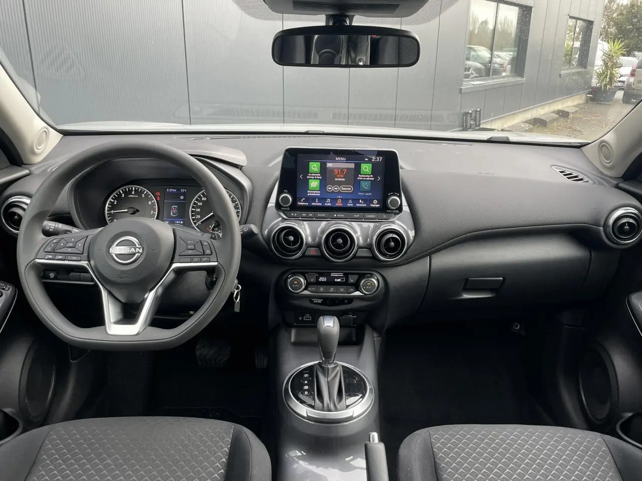 Vue frontale de l'habitacle noir du Nissan Juke 2024 avec volant multifonction et écran tactile central.