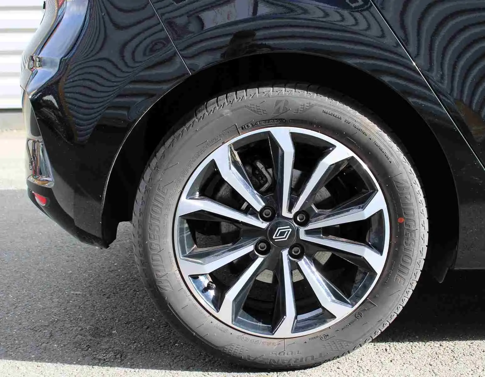 Gros plan sur la roue arrière droite d'une Renault Clio noire étoile métal avec jante alliage bicolore moderne.