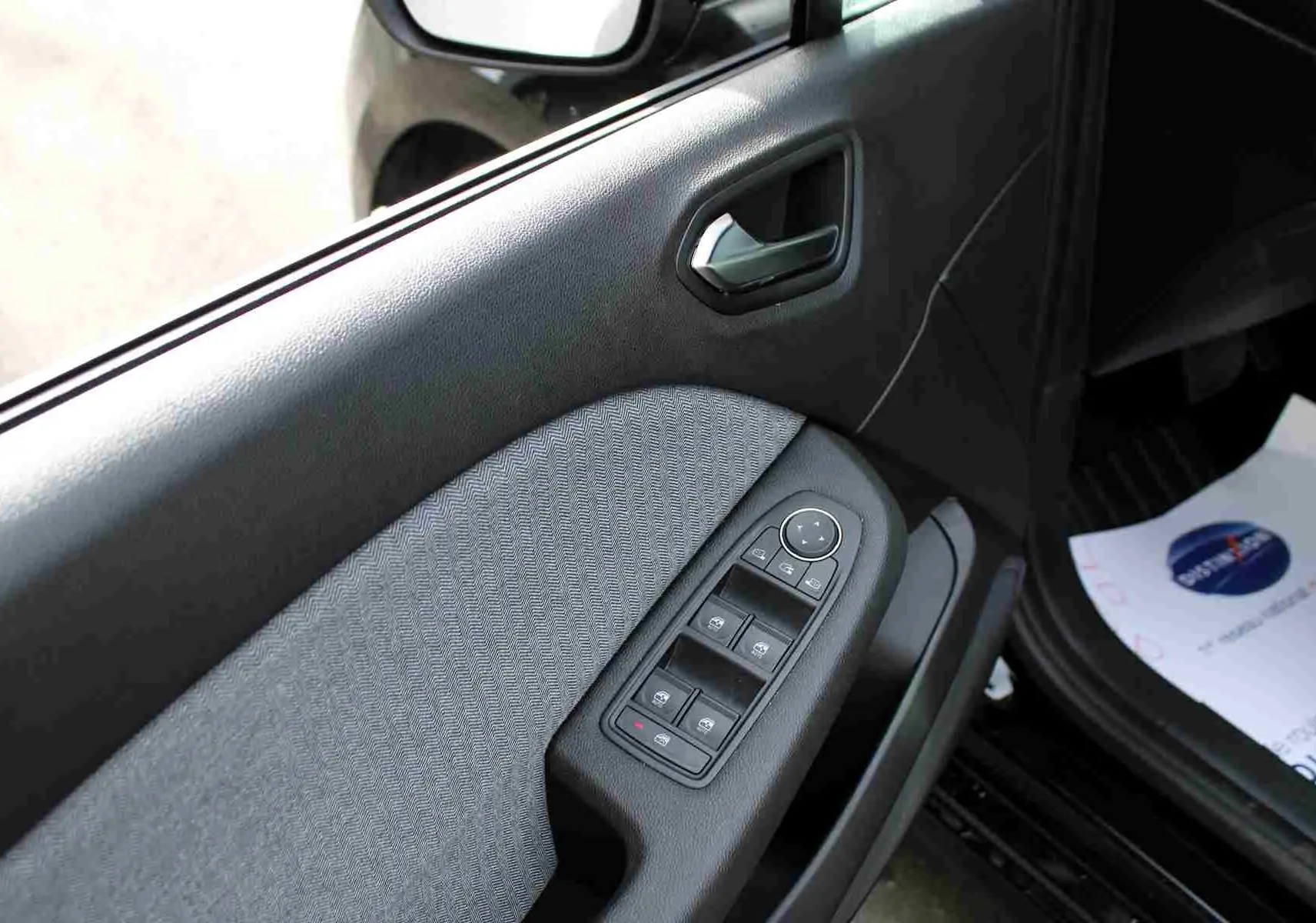 Gros plan sur la porte avant gauche de la Renault Clio 2025, montrant les commandes de vitres électriques et le tissu gris noir.