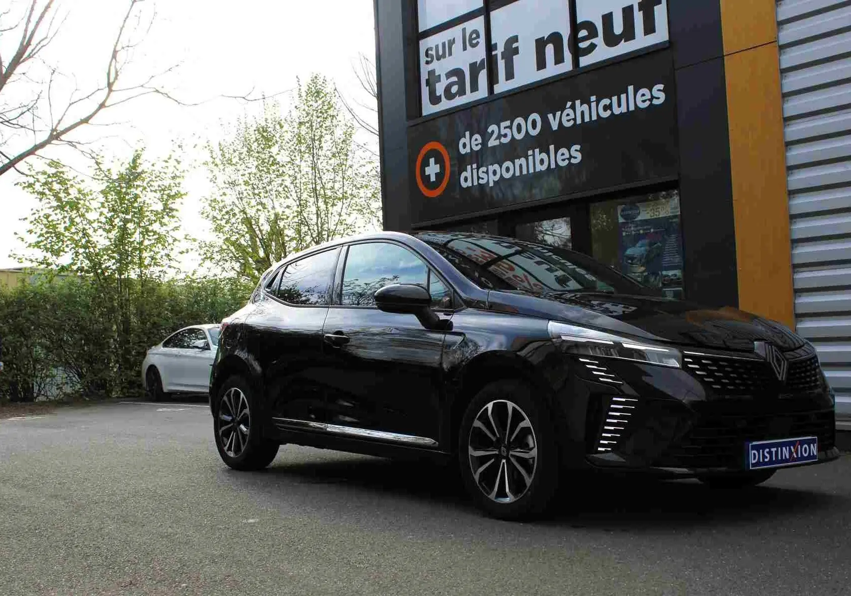 Renault Clio noire étoile métal vue 3/4 avant droit, avec feux LED et jantes alliage distinctives, stationnée devant un panneau publicitaire.