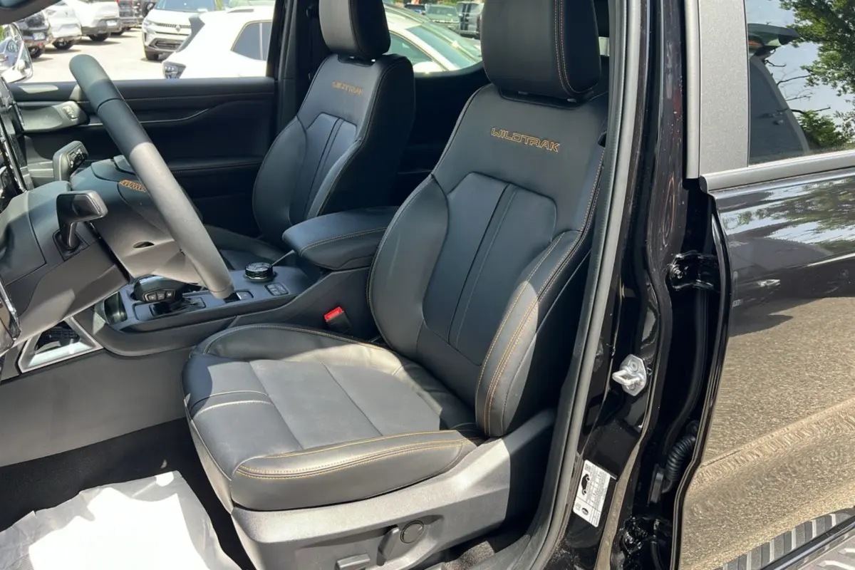 Vue intérieure côté conducteur du Ford Ranger Wildtrak 2.3 PHEV noir agate, sièges cuir avec surpiqûres orange et logo Wildtrak.