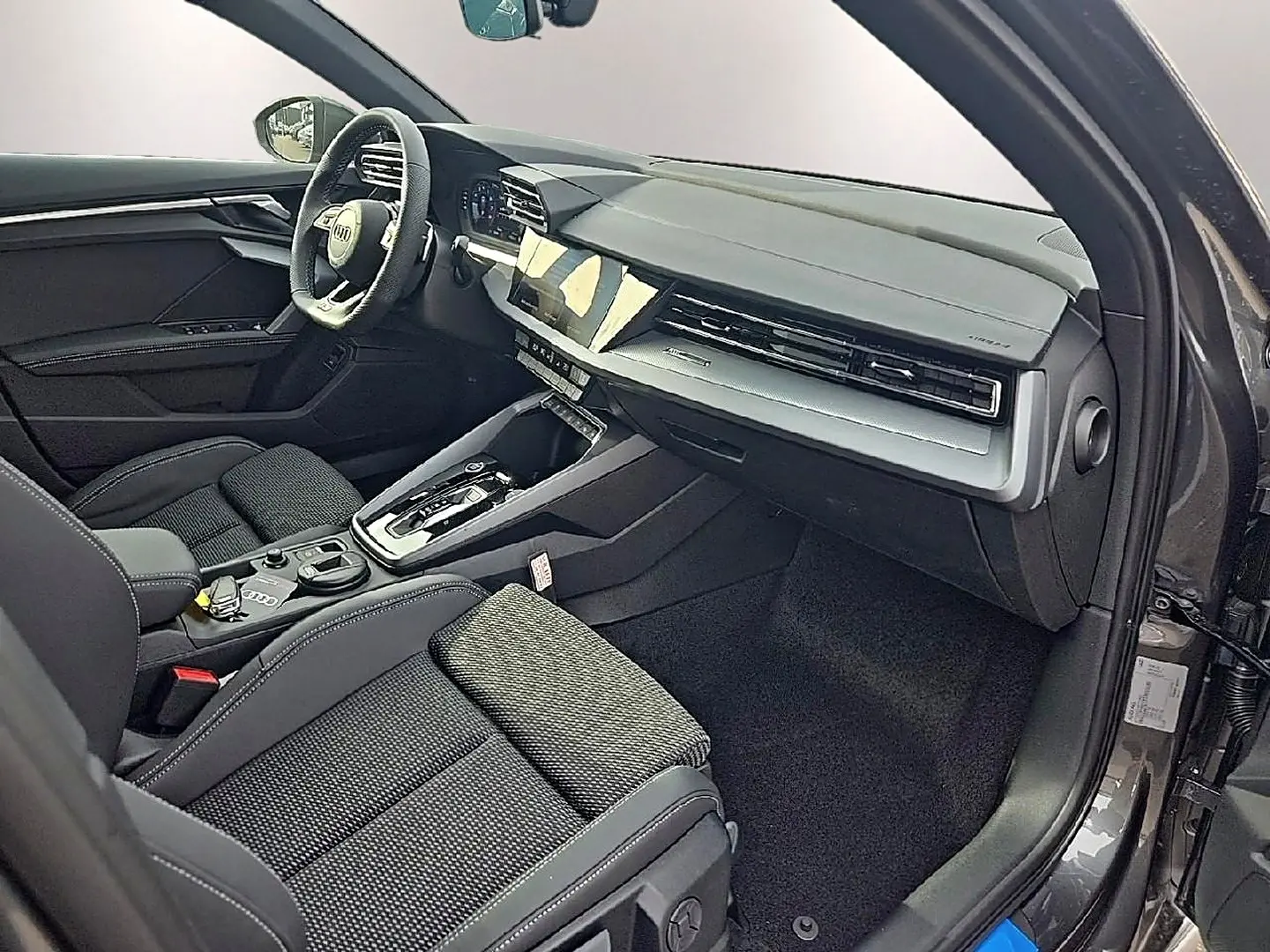 Intérieur avant droit de l'Audi A3 Sportback 2026, sièges tissu gris et tableau de bord moderne noir et gris.