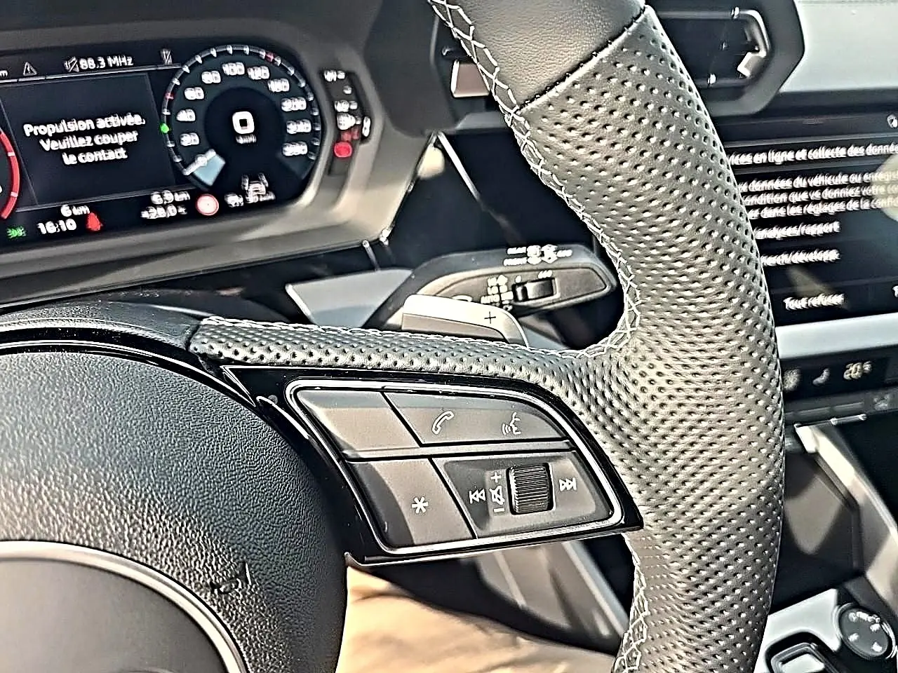 Gros plan sur le volant cuir perforé et les commandes multifonctions à gauche de l'Audi A3 Sportback 2026.