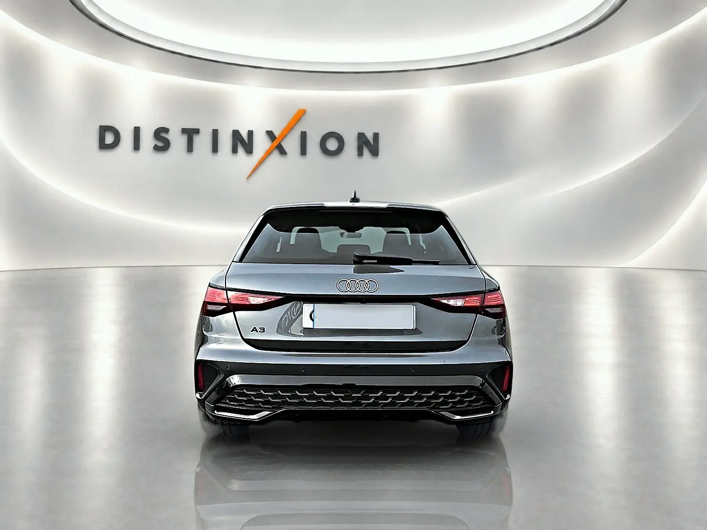 Vue arrière d'une Audi A3 Sportback 2026 gris Daytona, avec feux LED et diffuseur noir dans un showroom lumineux.