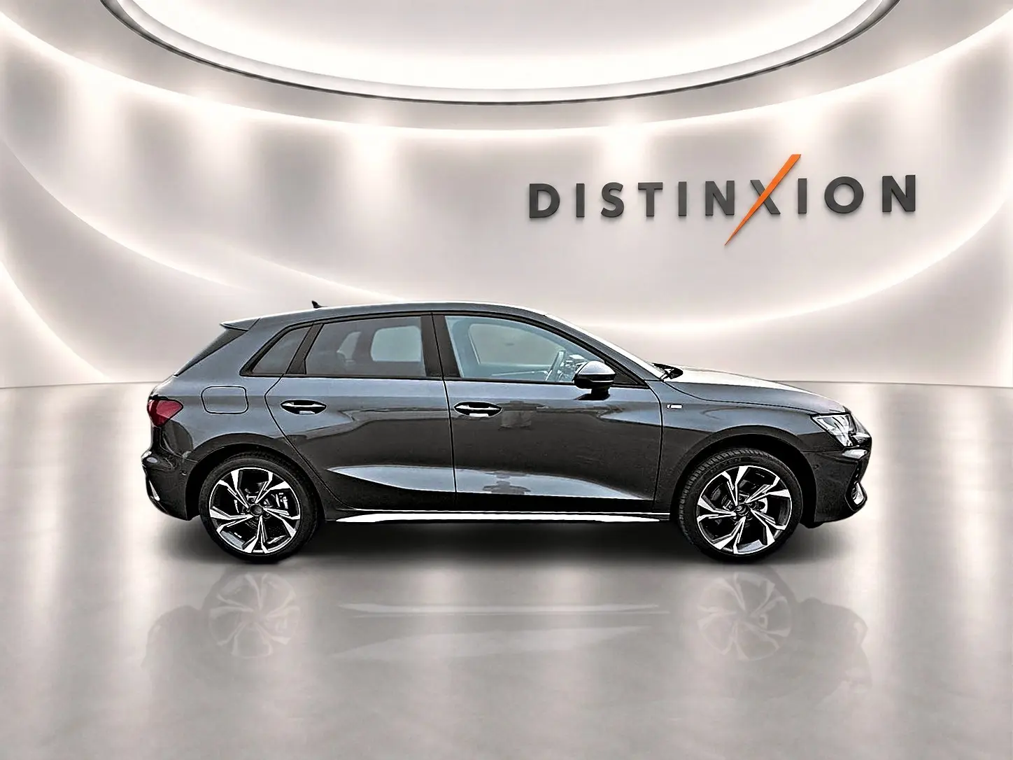 Audi A3 Sportback gris Daytona vue de profil côté gauche dans un studio lumineux avec logo Distinxion en arrière-plan.