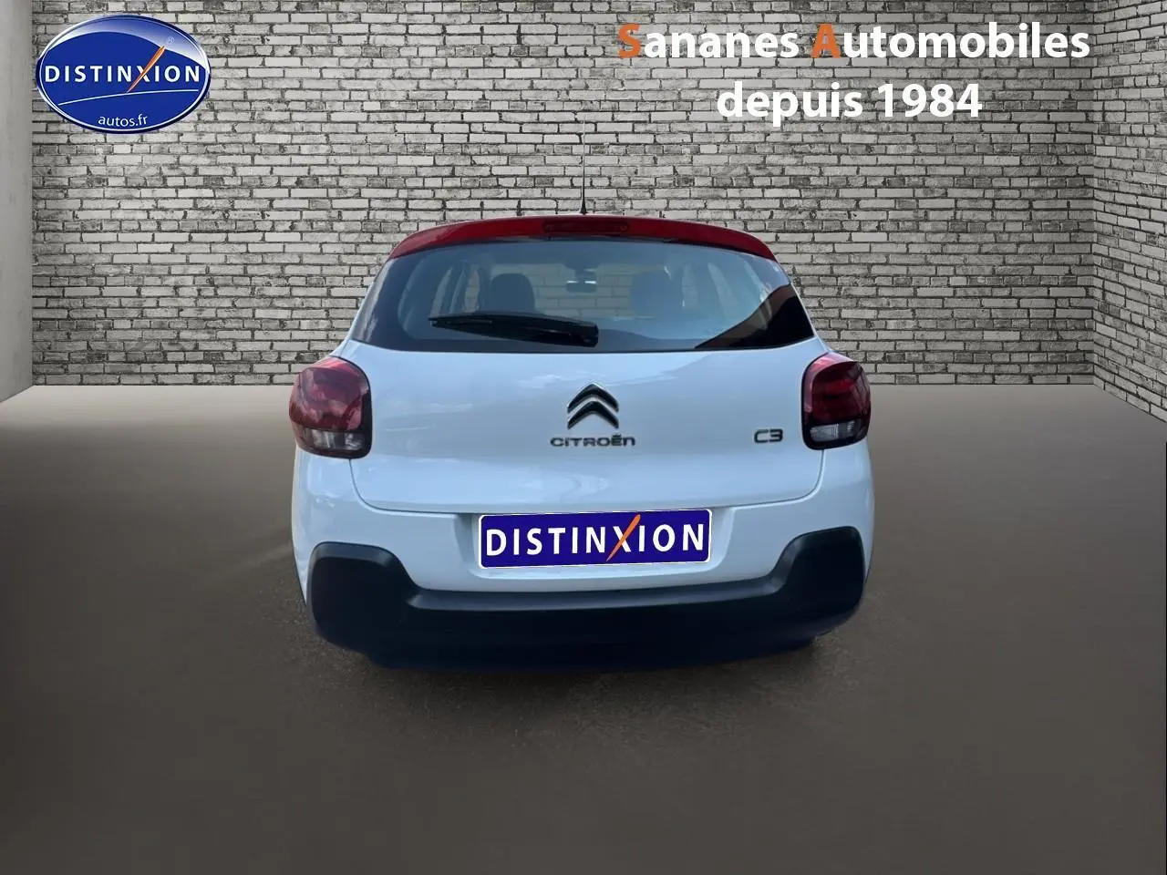 Vue arrière d'une Citroën C3 2023 blanche avec toit rouge et logo distinctif sur fond urbain en briques.