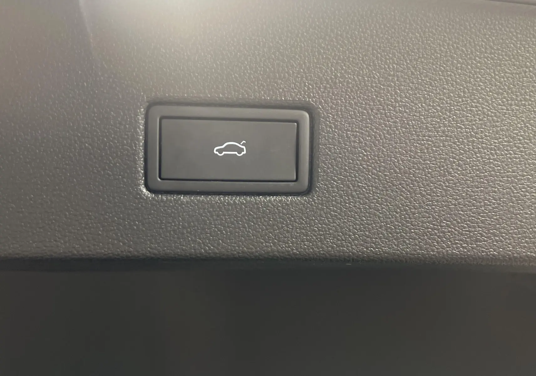Bouton d'ouverture électrique du coffre sur la garniture intérieure d'un Volkswagen T-Roc 1.5 TSI R-Line 2024 gris Pyrite.