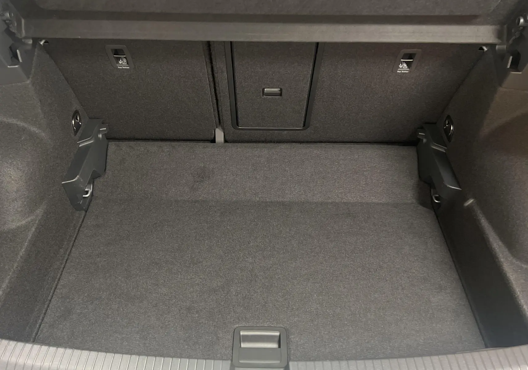 Coffre spacieux du Volkswagen T-Roc 2024, finition R-Line, avec revêtement intérieur gris foncé et compartiments latéraux.