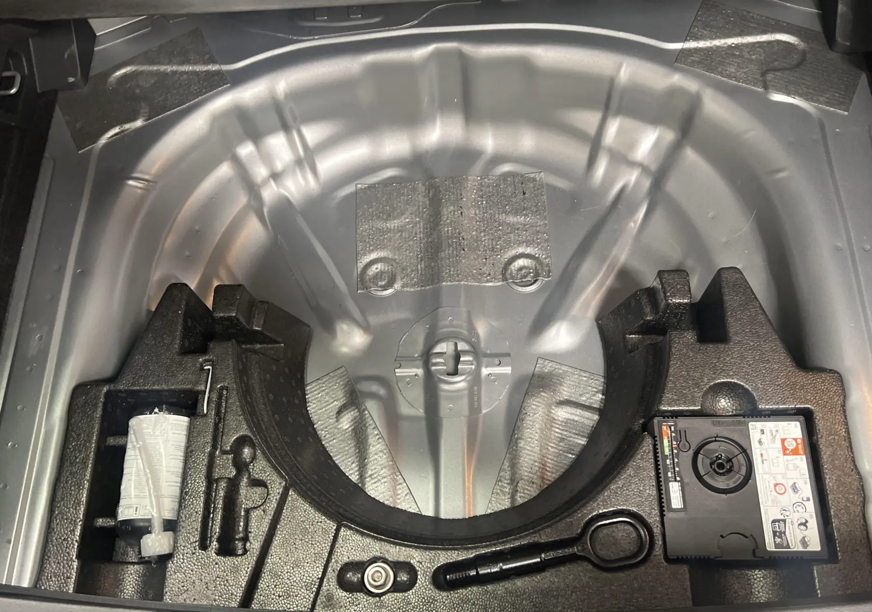 Coffre ouvert montrant le rangement sous plancher avec kit de réparation et espace pour roue de secours du Volkswagen T-Roc.