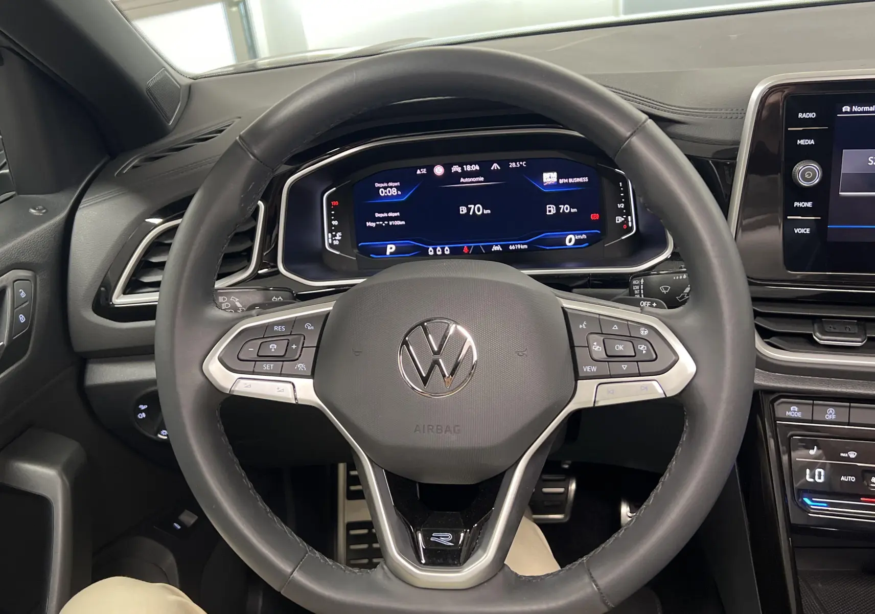 Vue intérieure centrée sur le volant cuir du Volkswagen T-Roc 2024 avec tableau de bord numérique et écran tactile.