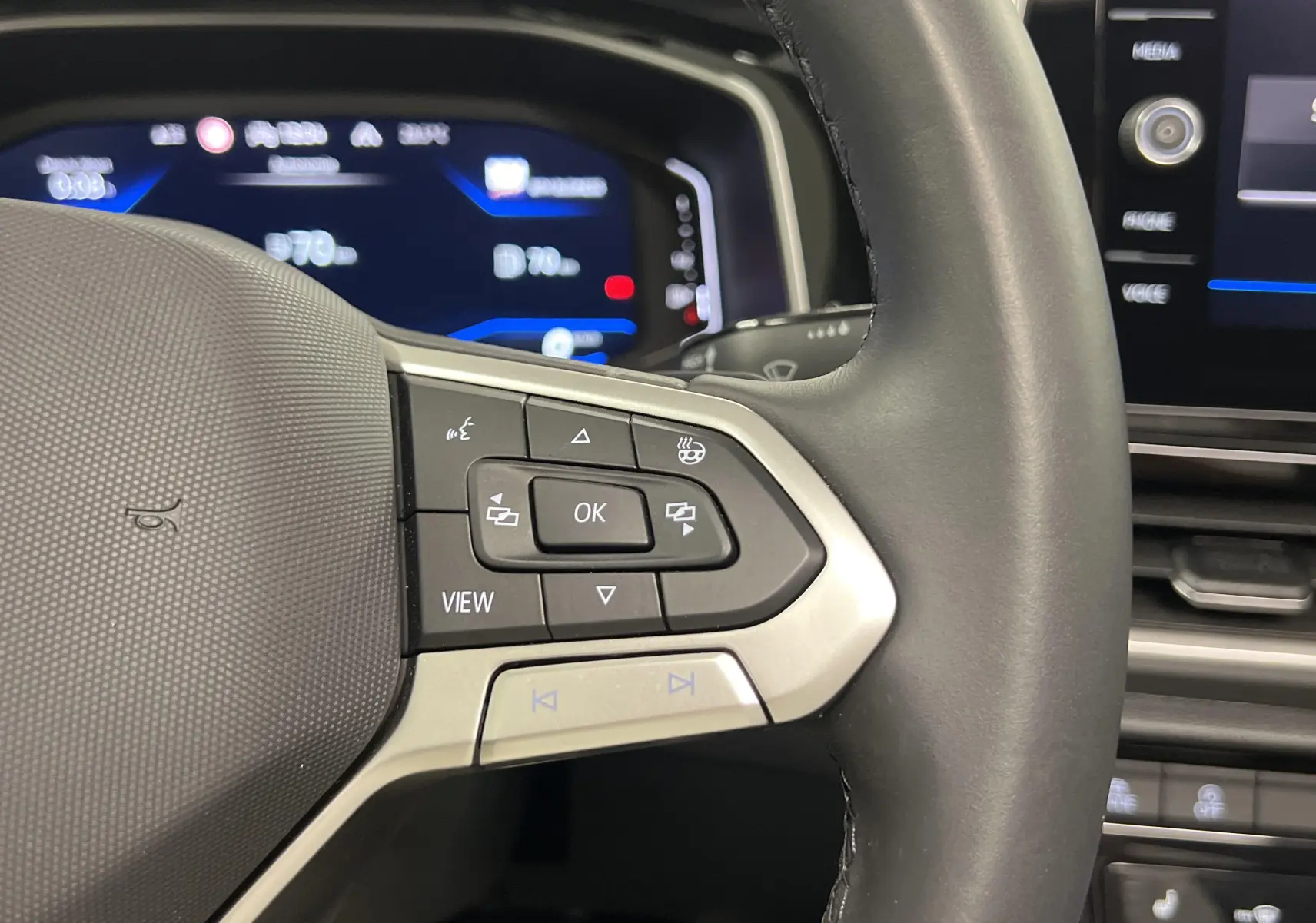 Gros plan sur le volant du Volkswagen T-Roc 2024 avec commandes intégrées et tableau de bord numérique en arrière-plan.