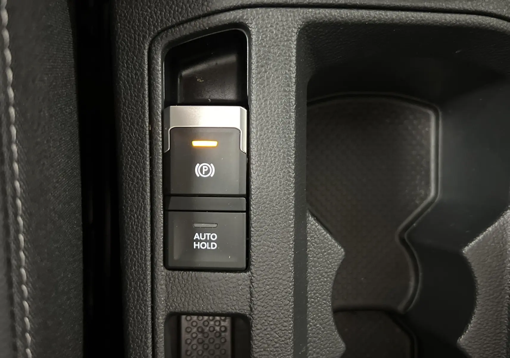 Gros plan sur les commandes de frein à main électrique et auto hold dans l'habitacle du Volkswagen T-Roc gris Pyrite 2024.