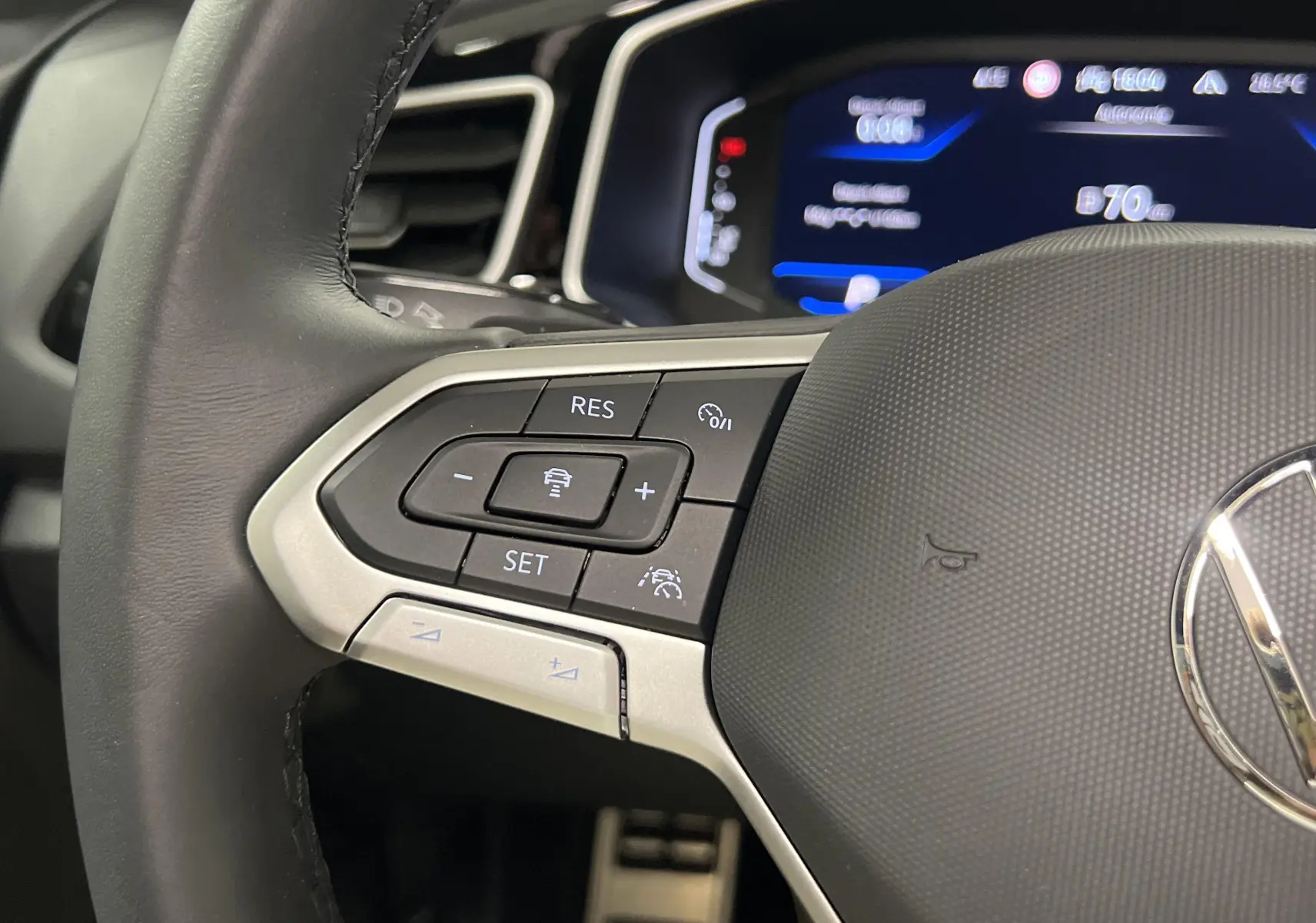 Gros plan sur le volant noir du Volkswagen T-Roc 2024 avec commandes intégrées et tableau de bord numérique bleu.