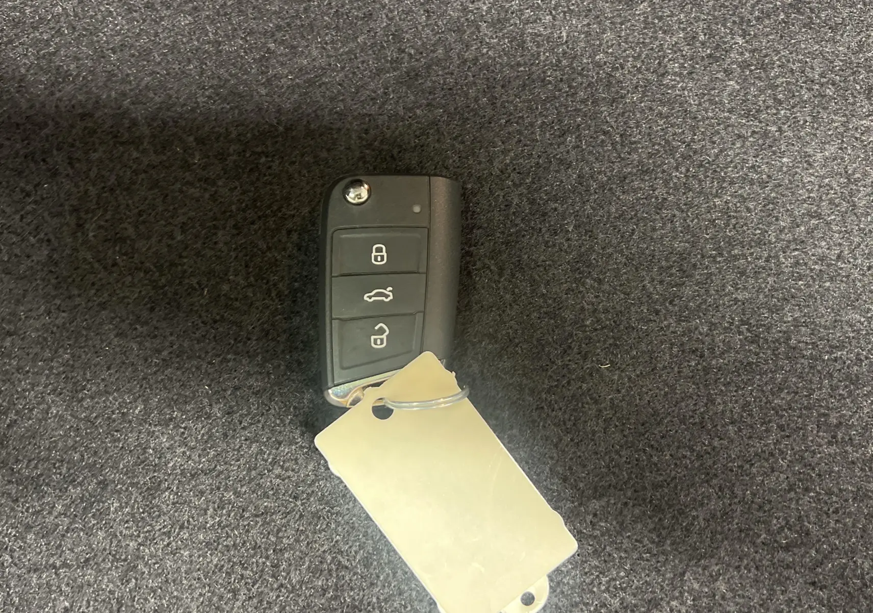 Télécommande noire Volkswagen T-Roc 2024 avec boutons verrouillage, coffre et déverrouillage sur fond gris.