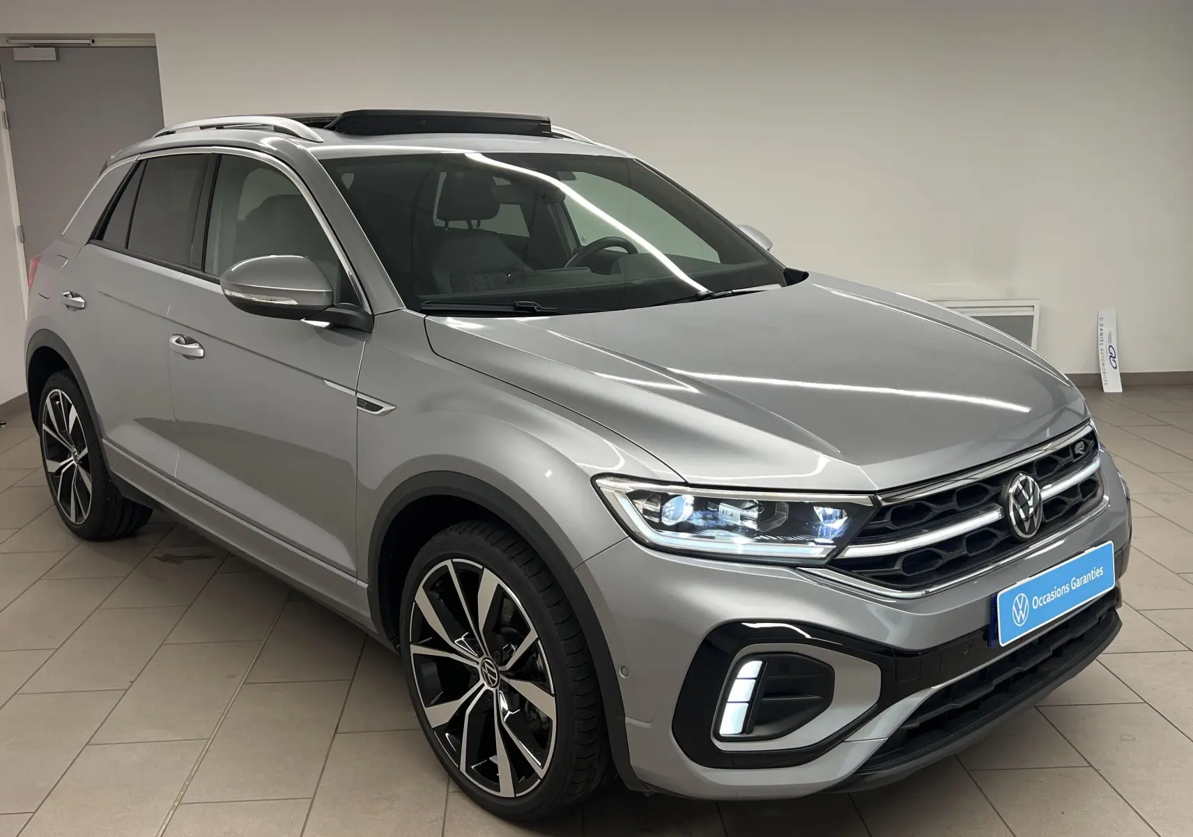 Volkswagen T-Roc gris pyrite en 3/4 avant droit avec jantes 19 pouces et toit ouvrant panoramique visible.