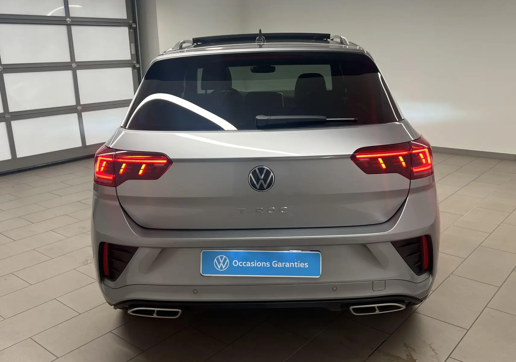 Vue arrière d'un Volkswagen T-Roc gris pyrite 2024 avec feux Matrix LED allumés et double sortie d'échappement rectangulaire.
