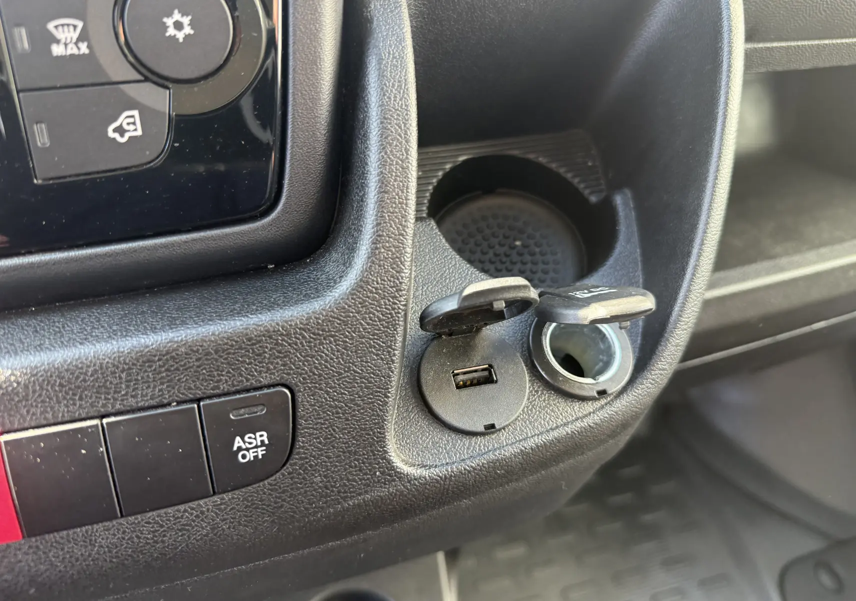 Gros plan sur la console centrale noire de l'Opel Movano Fourgon 2023, montrant prise USB et allume-cigare ouverts.