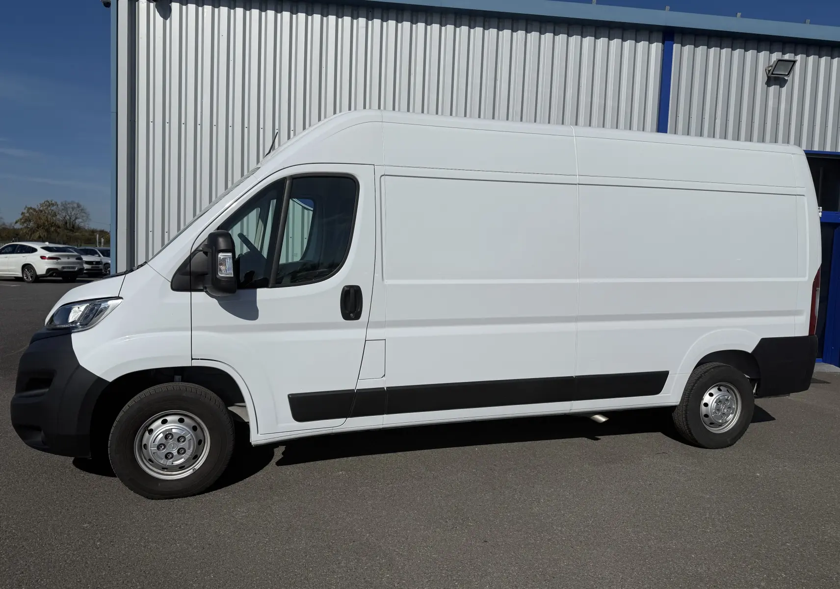 Vue 3/4 avant droit d’un Opel Movano Fourgon blanc 2023 avec pare-chocs noir et calandre chromée, stationné devant un bâtiment.