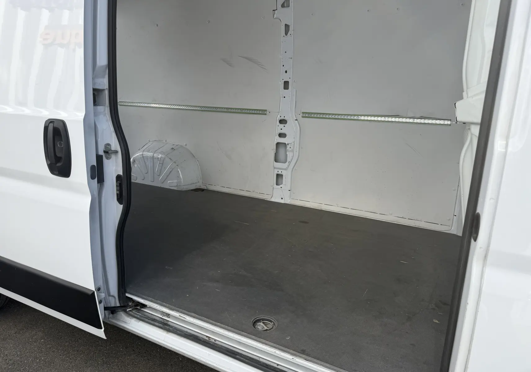 Vue intérieure du fourgon blanc Opel Movano 2.2 BlueHDi 140 L3H2, montrant l’espace de chargement vide avec porte latérale ouverte.