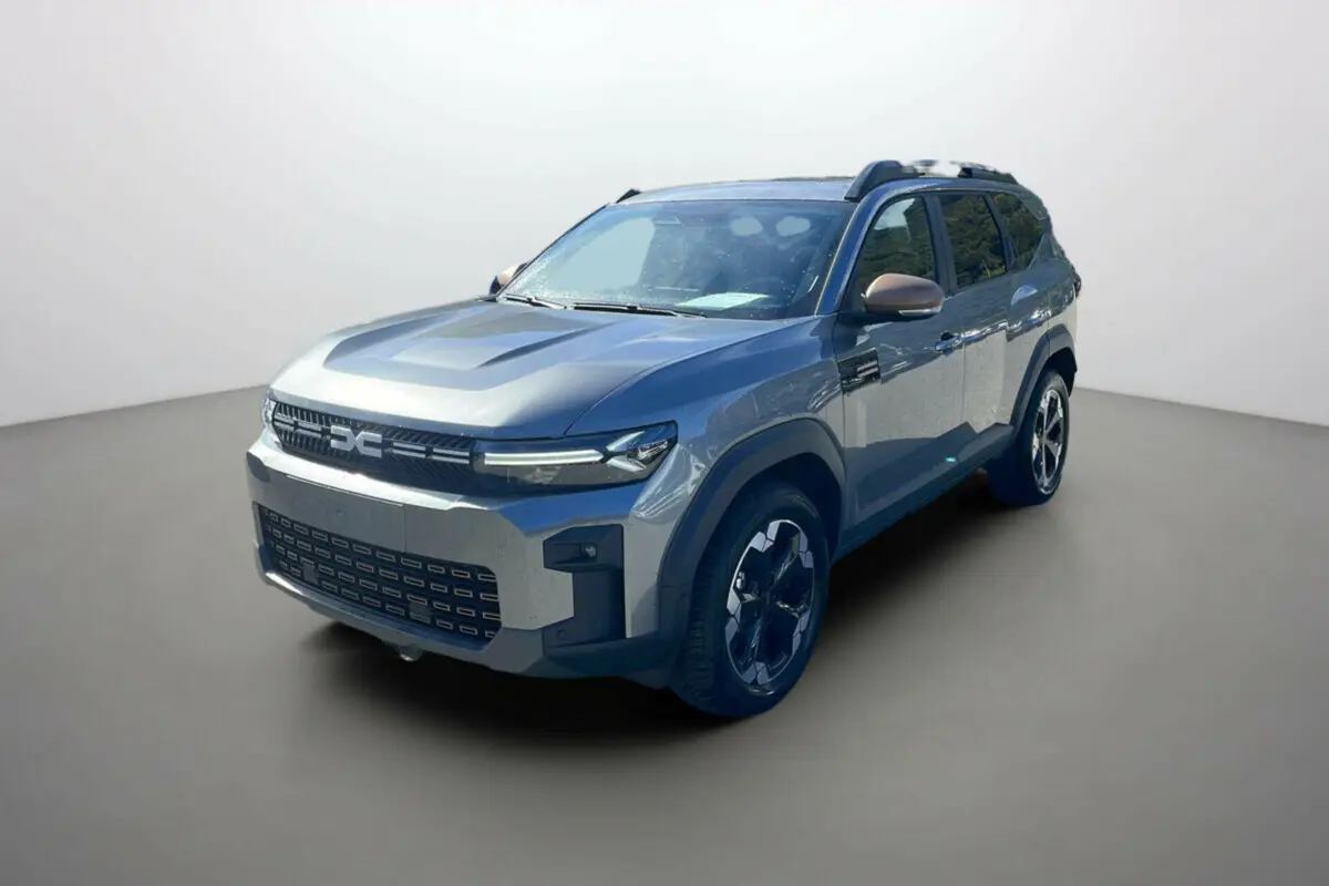 Dacia Bigster gris schiste en 3/4 avant droit avec jantes alu noires et barres de toit visibles.