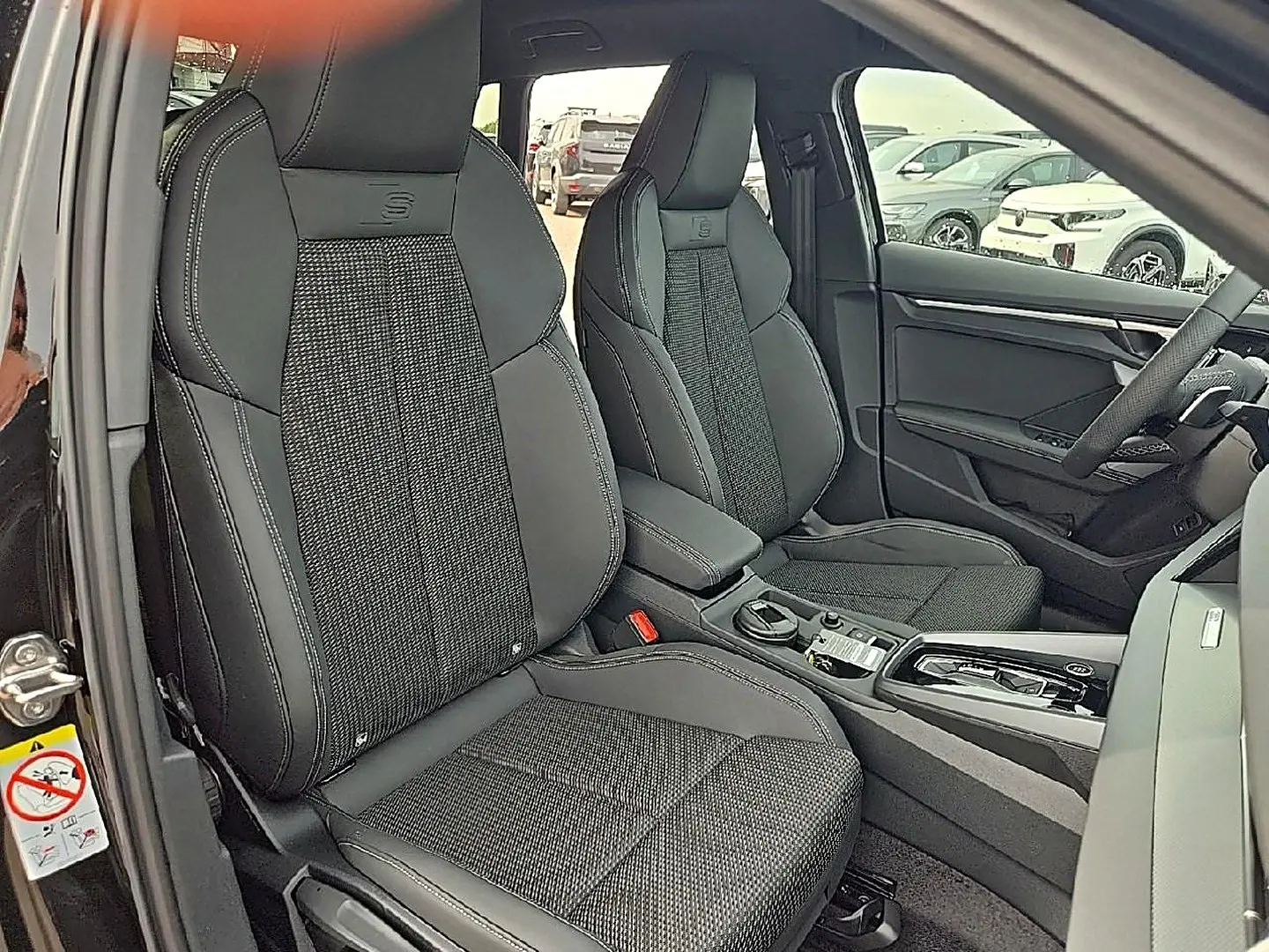Vue intérieure côté avant gauche de l’Audi A3 Sportback 2026 avec sièges sport noirs et console centrale moderne.