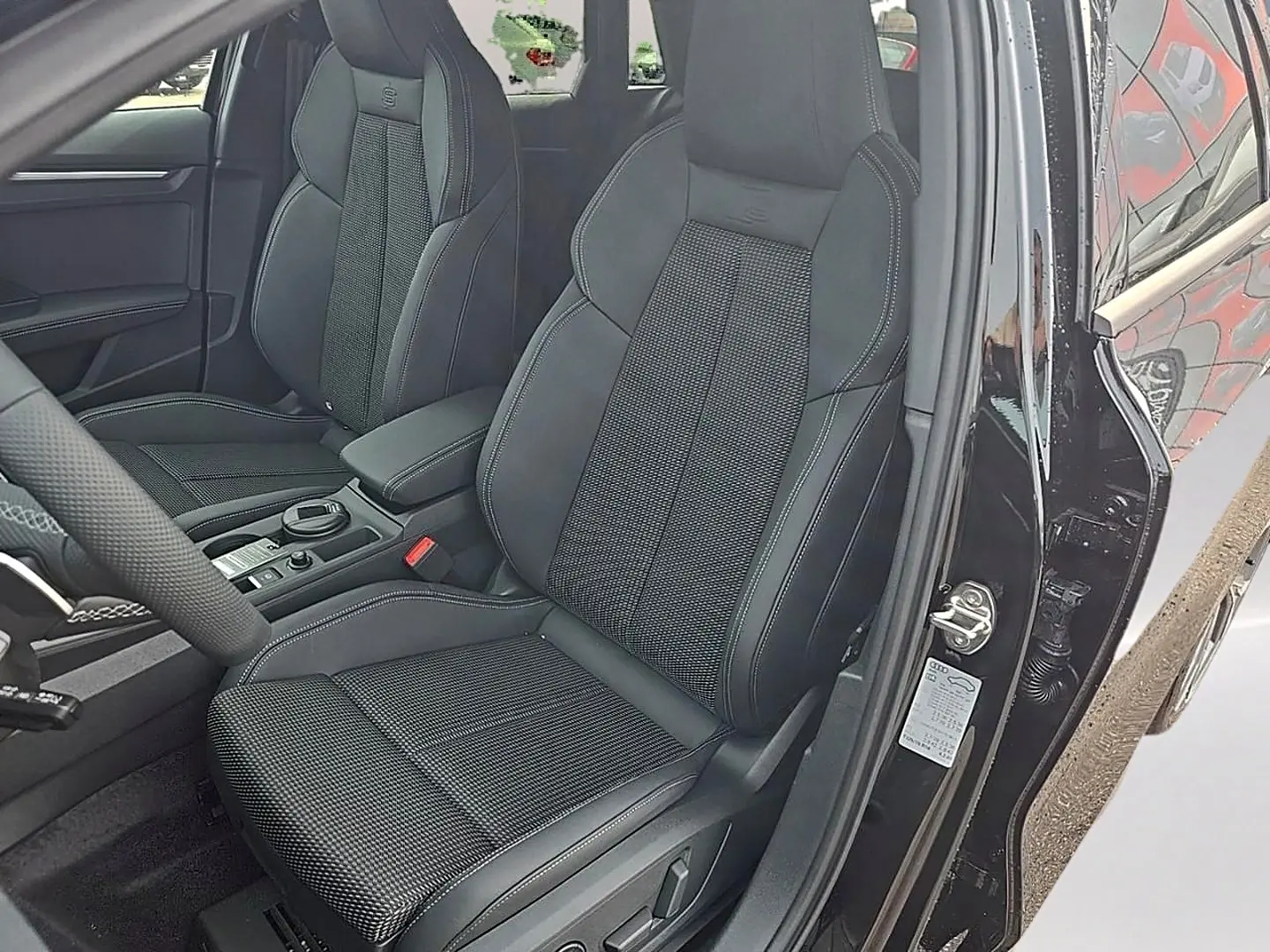 Vue intérieure côté conducteur de l'Audi A3 Sportback noir mythos, sièges sport avec surpiqûres blanches et accoudoir central.