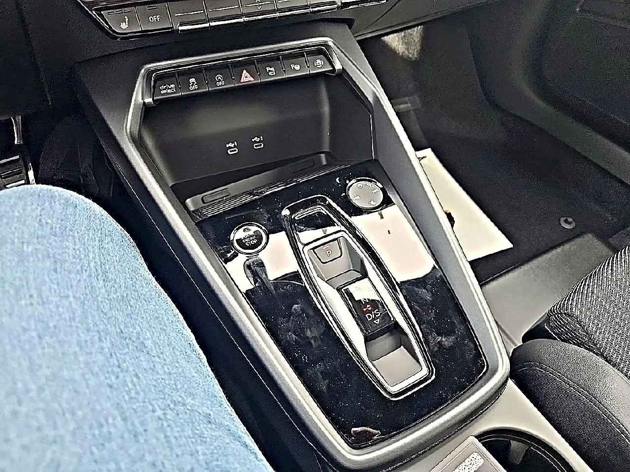 Vue rapprochée de la console centrale noire brillante de l’Audi A3 Sportback 2026 avec levier de vitesse automatique et commandes.