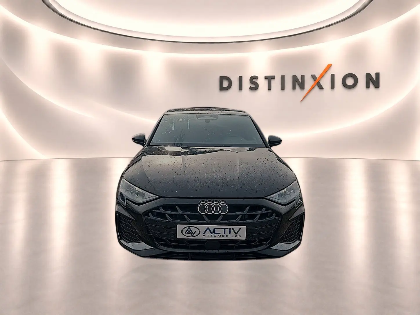 Vue avant d'une Audi A3 Sportback noire Mythos avec calandre S line et logo Audi visible sur fond lumineux Distinxion.