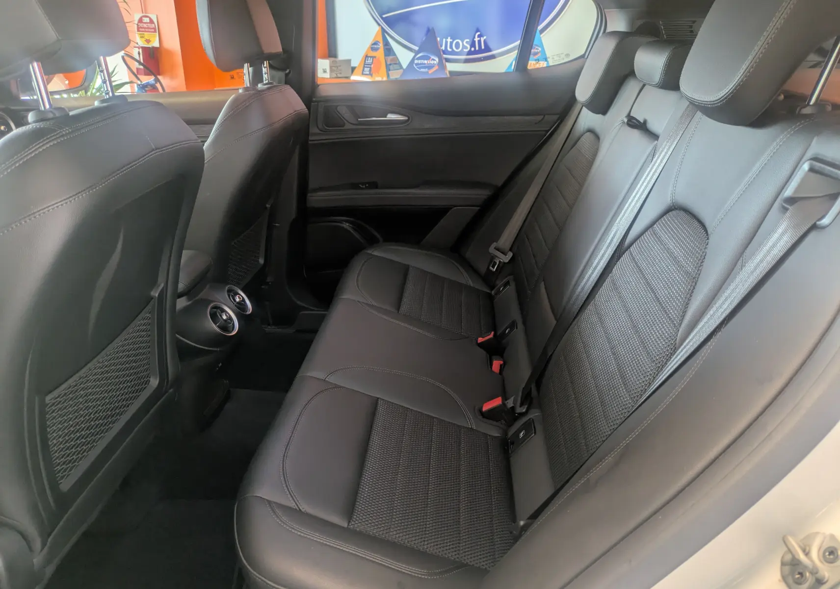 Vue latérale droite de l'intérieur arrière de l'Alfa Romeo Stelvio blanc, sièges en cuir noir et aérateurs centraux visibles.