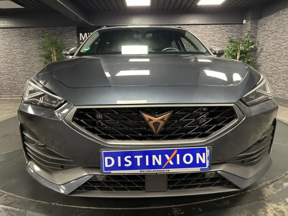 Vue frontale d'une CUPRA Leon Sportstourer gris magnétique avec calandre noire et logo cuivre distinctif.