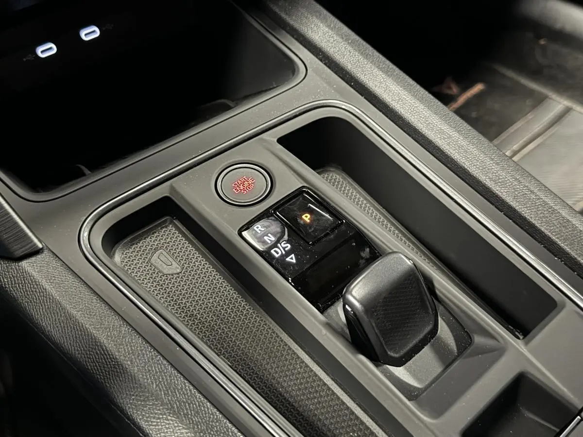 Gros plan sur la console centrale noire du CUPRA Leon Sportstourer 2024 avec levier de boîte auto et bouton start/stop rouge.