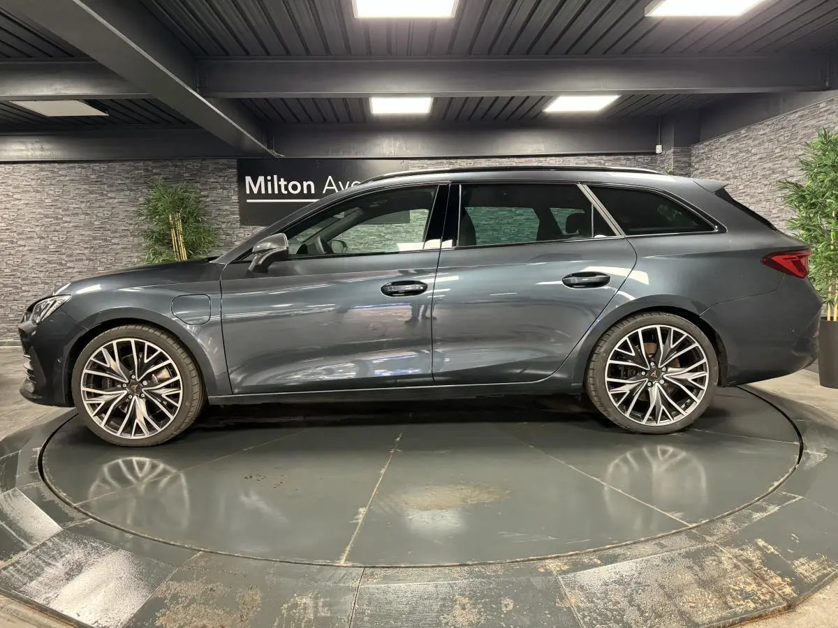 Profil droit d'une CUPRA Leon Sportstourer 1.4 e-Hybrid 245 gris magnétique avec jantes alliage 19 pouces dans un showroom.