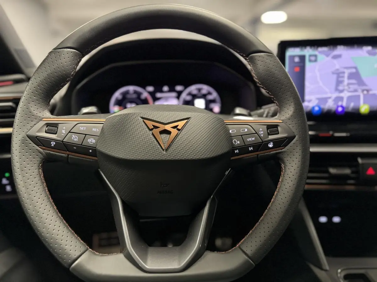 Volant perforé noir avec logo CUPRA cuivre au centre, tableau de bord digital et écran tactile de navigation visible en arrière-plan