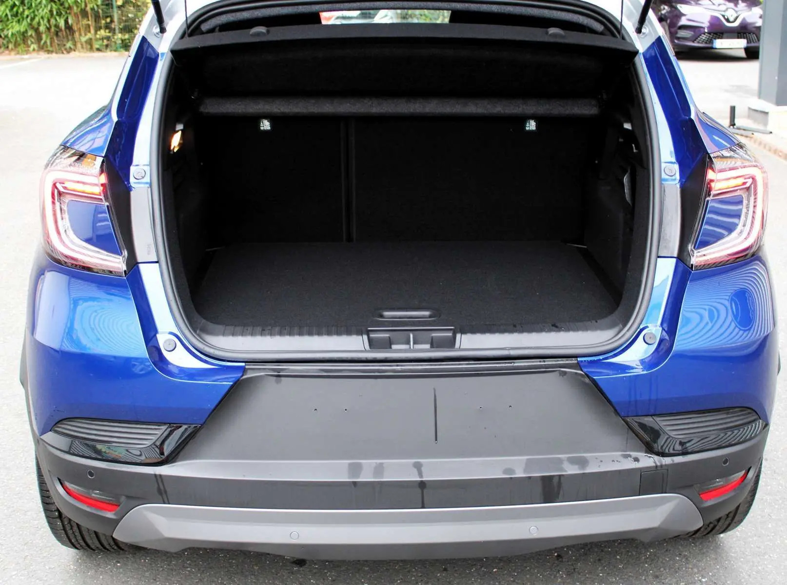 Coffre ouvert vu de l'arrière d'un Renault Captur bleu Iron Metal avec toit gris, feux arrière allumés.