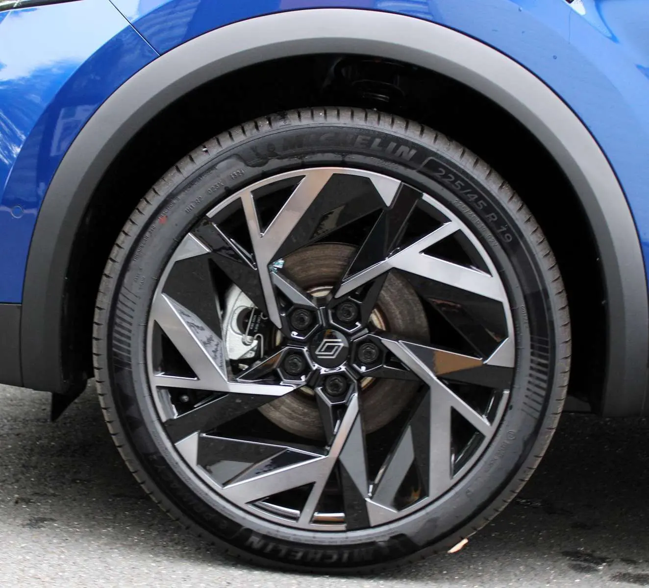 Gros plan sur la roue avant gauche du Renault Captur bleu Iron Metal avec jante alliage noire et argentée au design géométrique.