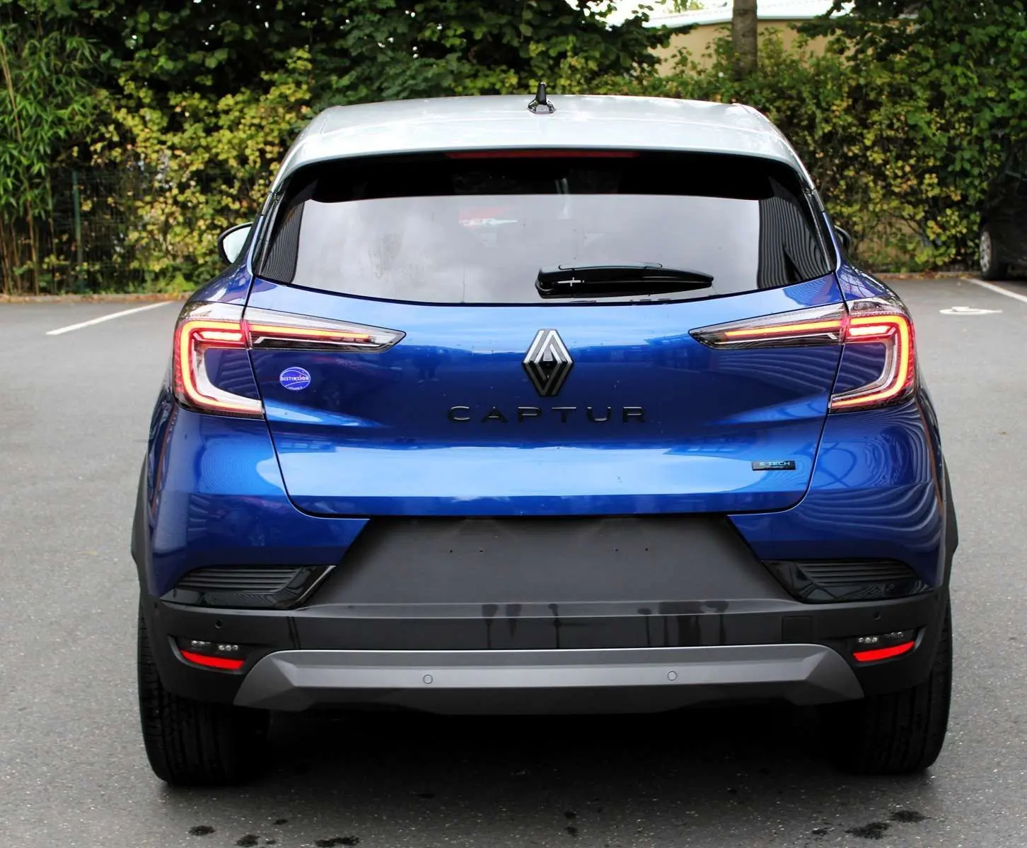 Vue arrière d'un Renault Captur bleu Iron Metal avec toit gris, feux LED allumés et logo central bien visible.