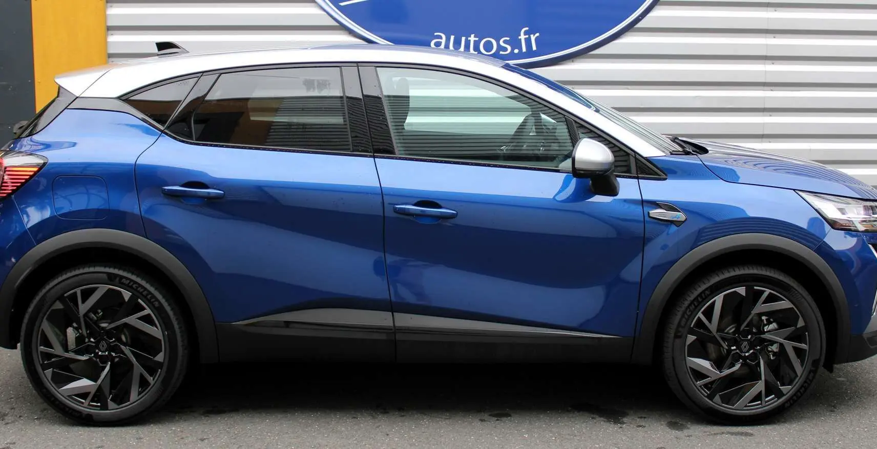 Profil côté gauche du Renault Captur 2025 bleu Iron Metal avec toit gris et jantes noires stylisées.