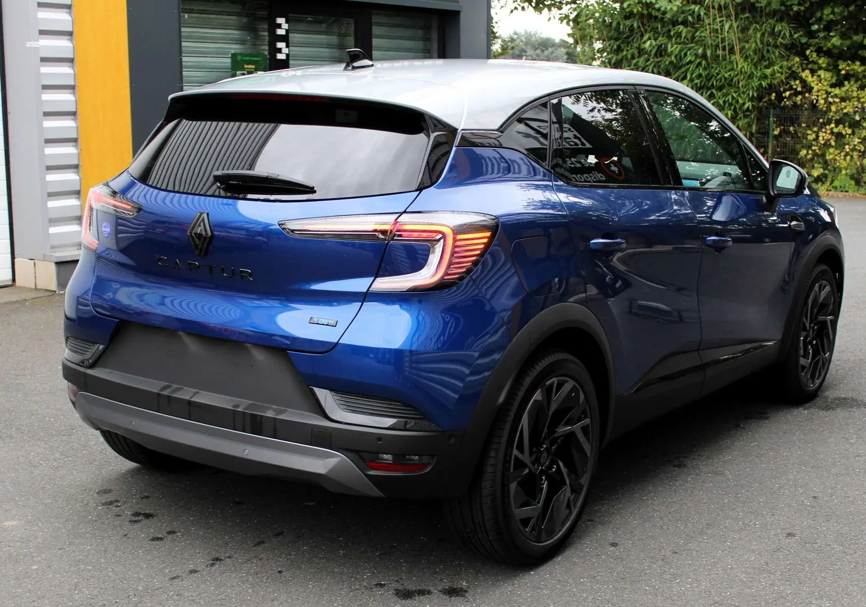 Vue 3/4 arrière droite du Renault Captur 2025 bleu Iron Metal avec toit gris et jantes noires distinctives.