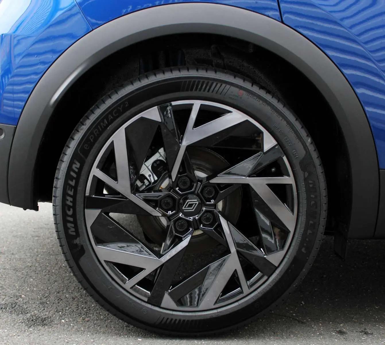 Gros plan sur la roue avant gauche du Renault Captur bleu Iron Metal avec jante alu bicolore au design géométrique.