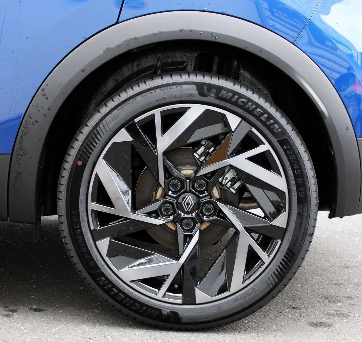 Gros plan sur la roue avant droite du Renault Captur bleu iron metal avec jante alliage noire et argentée au design géométrique.