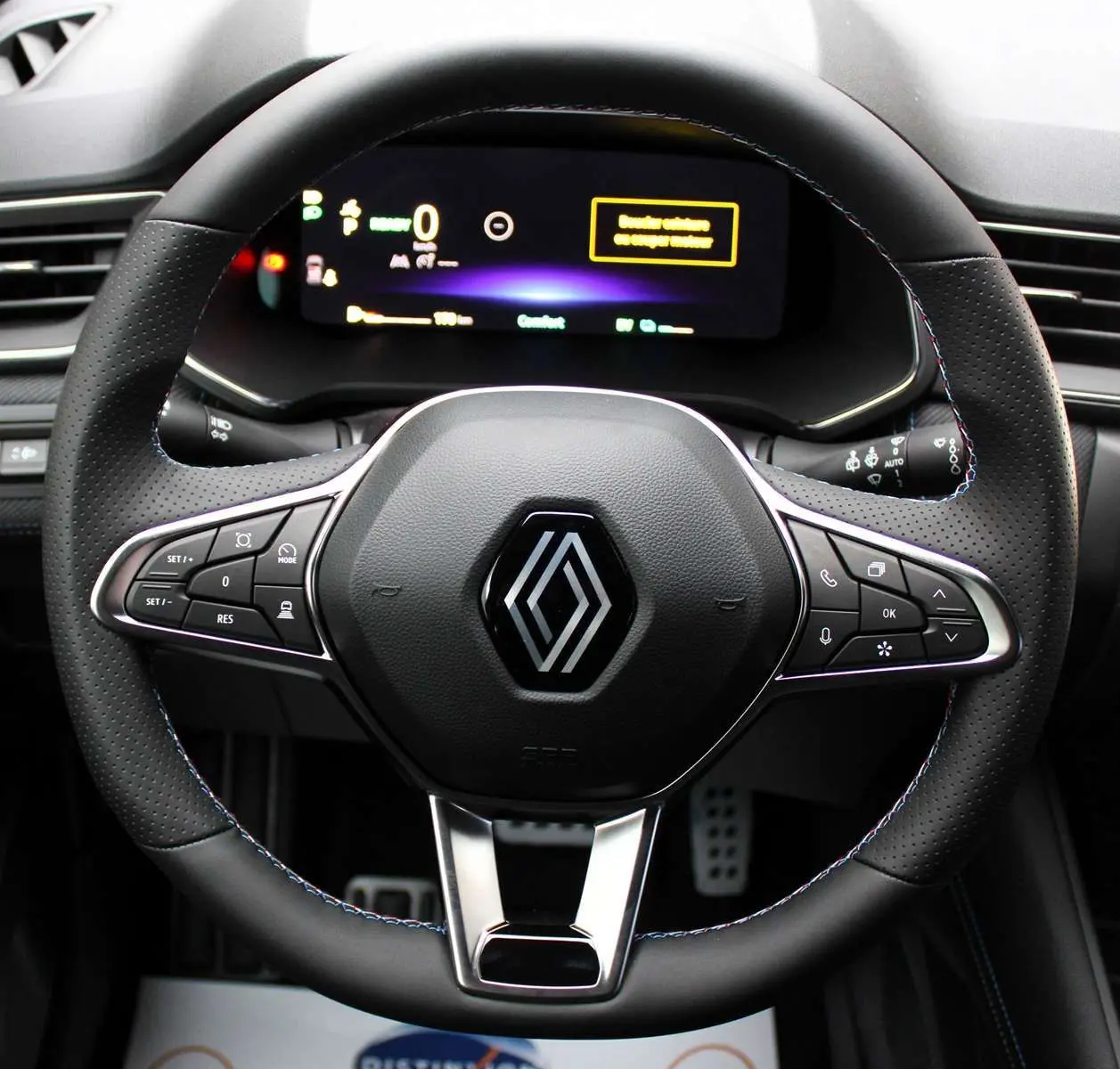 Gros plan sur le volant en cuir noir avec surpiqûres bleues du Renault Captur hybride, tableau de bord digital en arrière-plan.