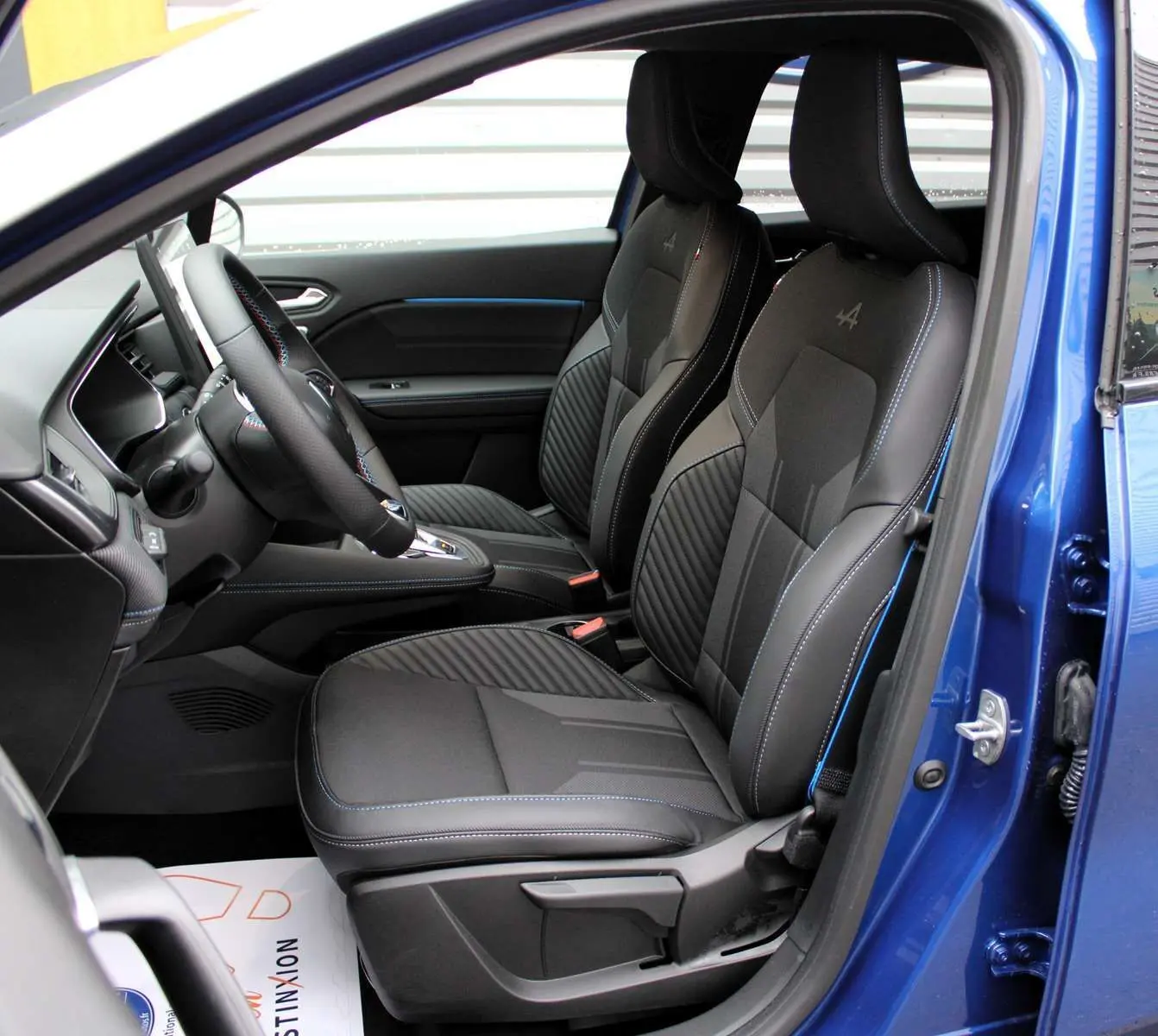 Vue intérieure côté gauche du Renault Captur 2025 bleu iron metal, sièges noirs avec surpiqûres bleues et logo Alpine brodé.