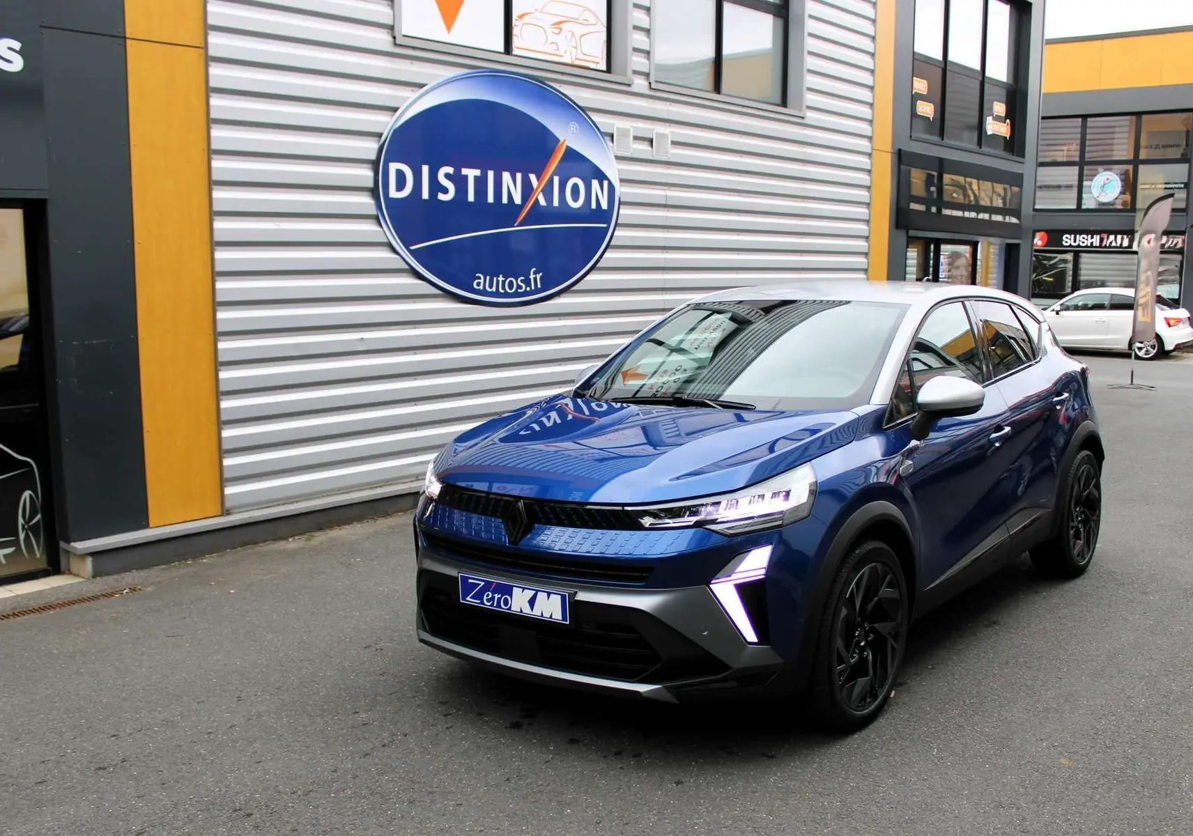 Renault Captur 2025 bleu Iron Metal avec toit gris, vue 3/4 avant droit, feux LED et jantes noires visibles.